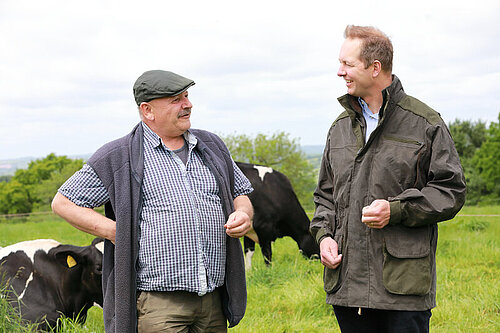 Richard Foord walking and talking with a farmer in a cow field